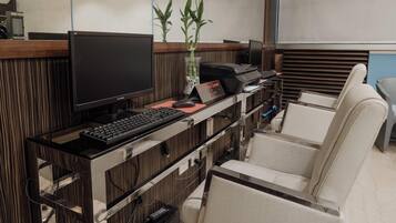 Mostrador de recepción con una computadora, una planta y un letrero que indica la zona central del hotel. Hay sillas y una barra con un teclado.