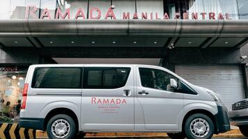 Una furgoneta blanca aparcada davant d'un edifici amb un cartell que diu 'RAMADA MANILA CENTRAL'.