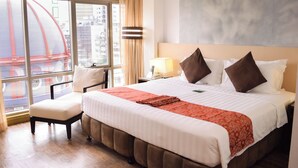 A hotel room with a large bed, a chair, a nightstand, and a window with a view of buildings. - Ramada by Wyndham Manila Central (Manila)