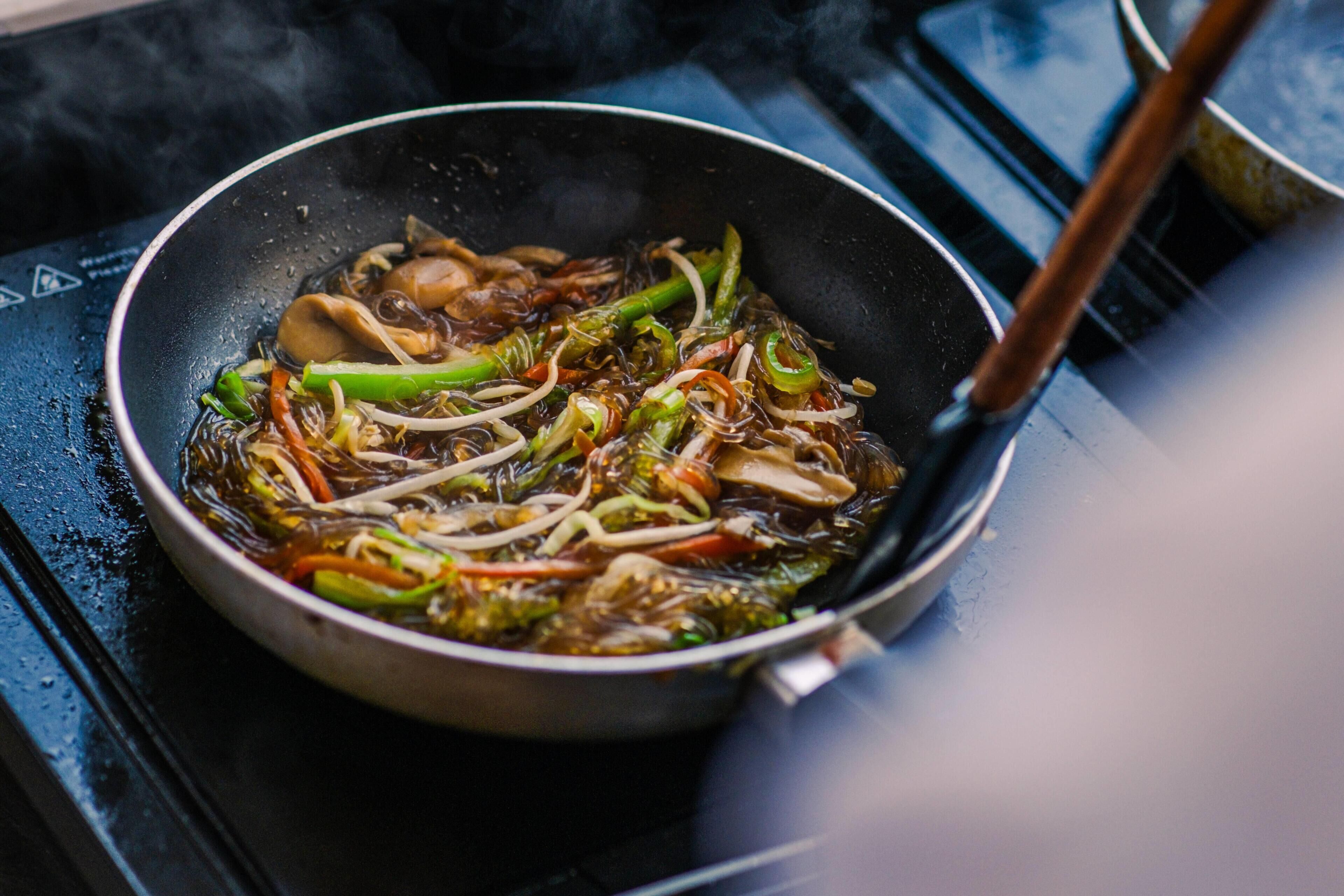 A pan with stir-fried vegetables and noodles on a stove.