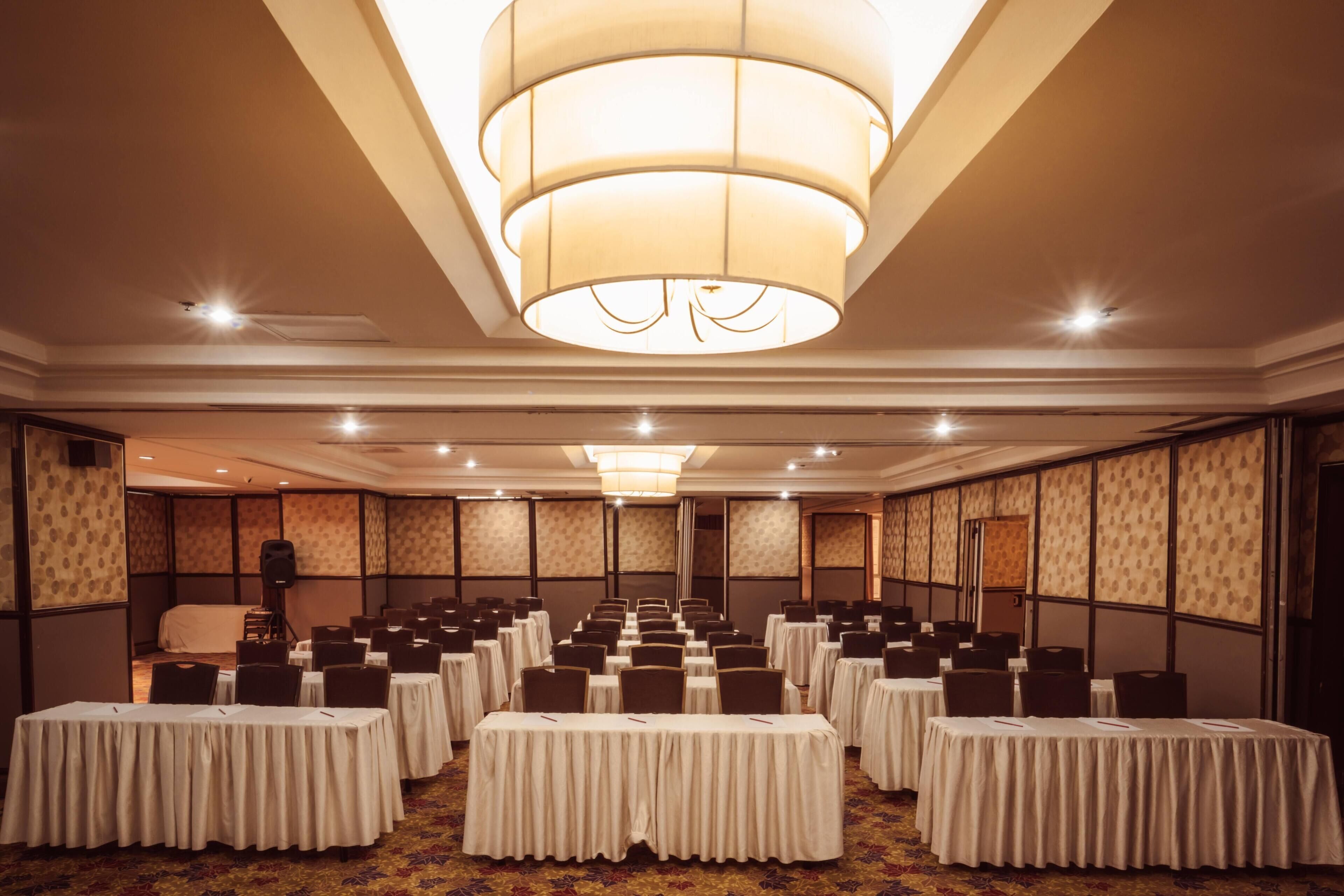 Un salón de conferencias con mesas y sillas, una gran lámpara de araña y paredes con diseño.