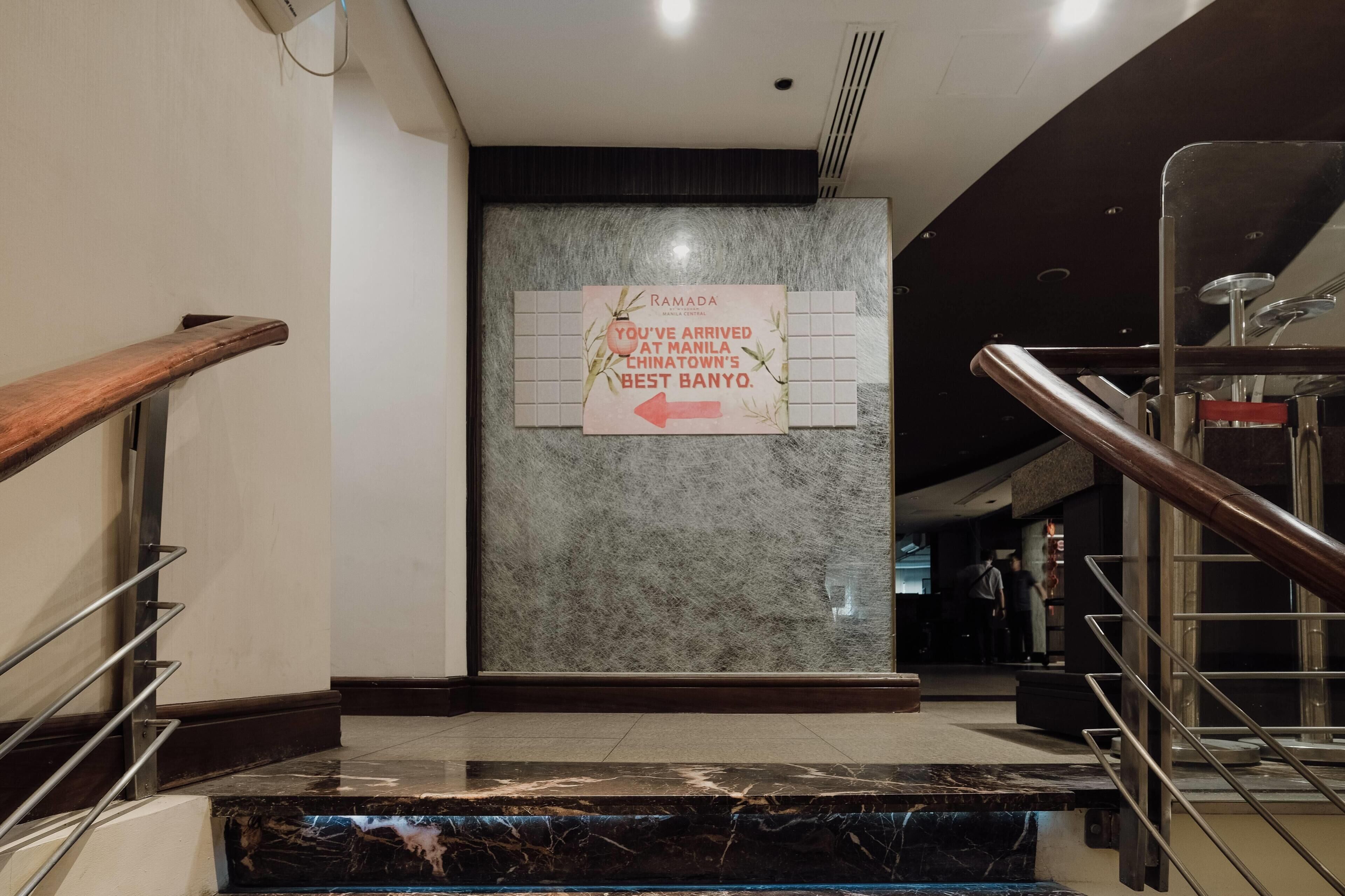 A marble staircase with metal railings leading to a lobby area featuring a sign indicating the arrival at Manila Chinatown's Best Banyo.