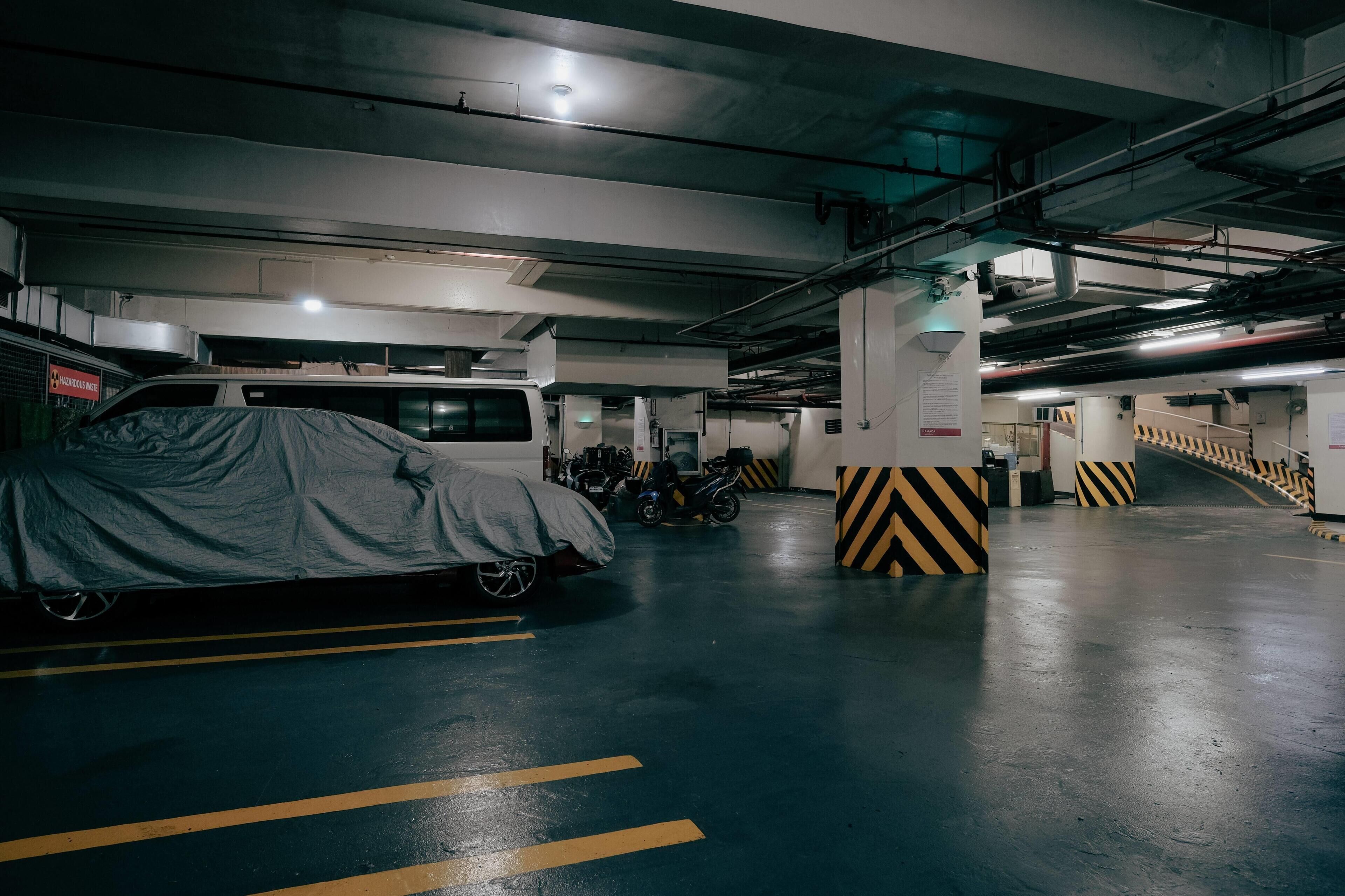 A parking garage with a covered car and a motorcycle, concrete pillars, and yellow parking lines.