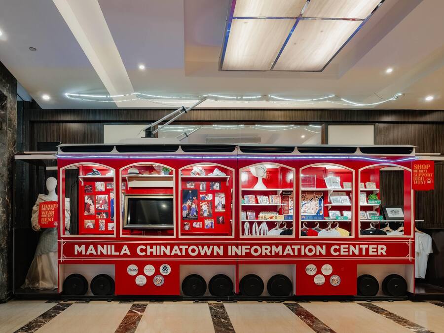 A red information kiosk with a mannequin, labeled 'MANILA CHINATOWN INFORMATION CENTER,' featuring various informational displays and a digital screen.