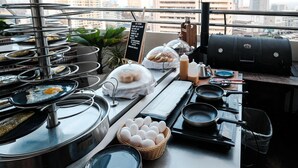 A buffet setup with various food items, a grill, and a view of the cityscape. - Ramada by Wyndham Manila Central (Manila)