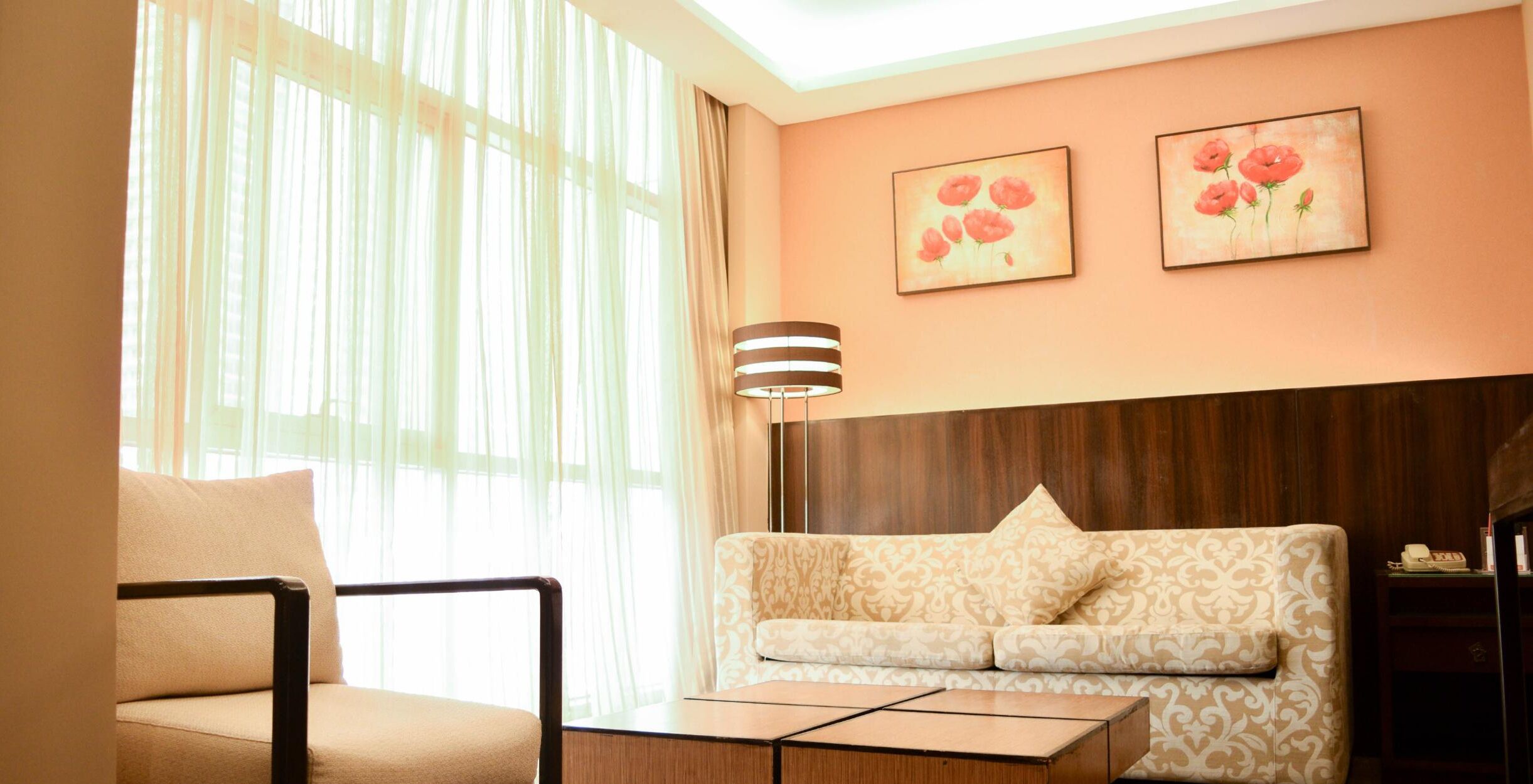 Une chambre d’hôtel avec un canapé, un fauteuil, une lampe et deux tableaux au mur.