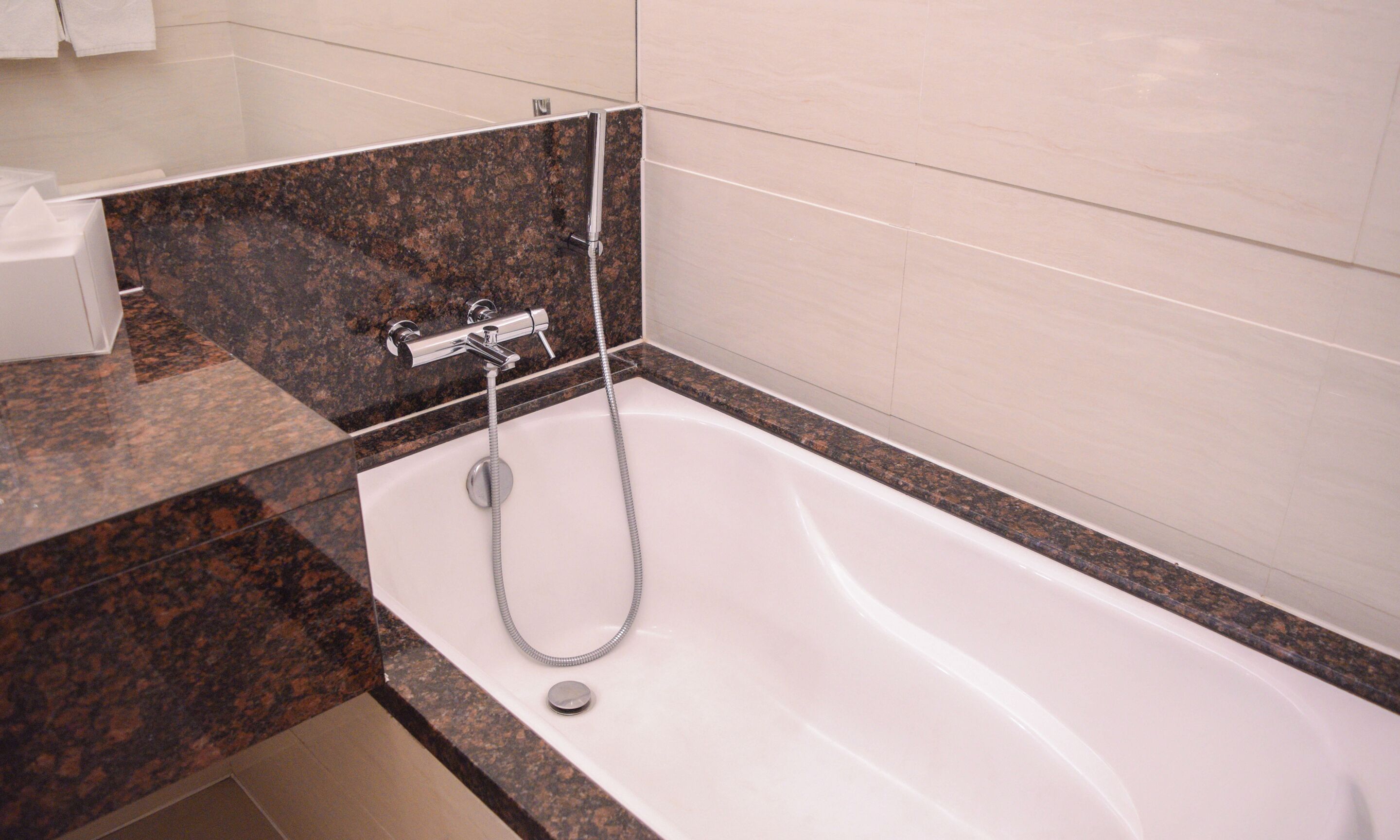 Un baño moderno con una bañera blanca, encimeras de granito y un cabezal de ducha cromado.