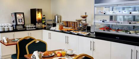 A breakfast area with a coffee machine, a fruit display, and a buffet counter.