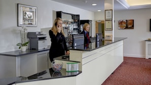 A reception desk with a printer, a glass display case with bottles, and framed artwork on the wall. - Best Western London Highbury (London)