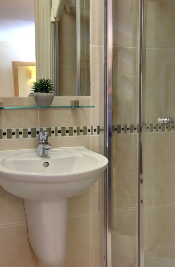 Un baño con un lavamanos blanco, cabina de ducha de vidrio y salpicadero de azulejos.