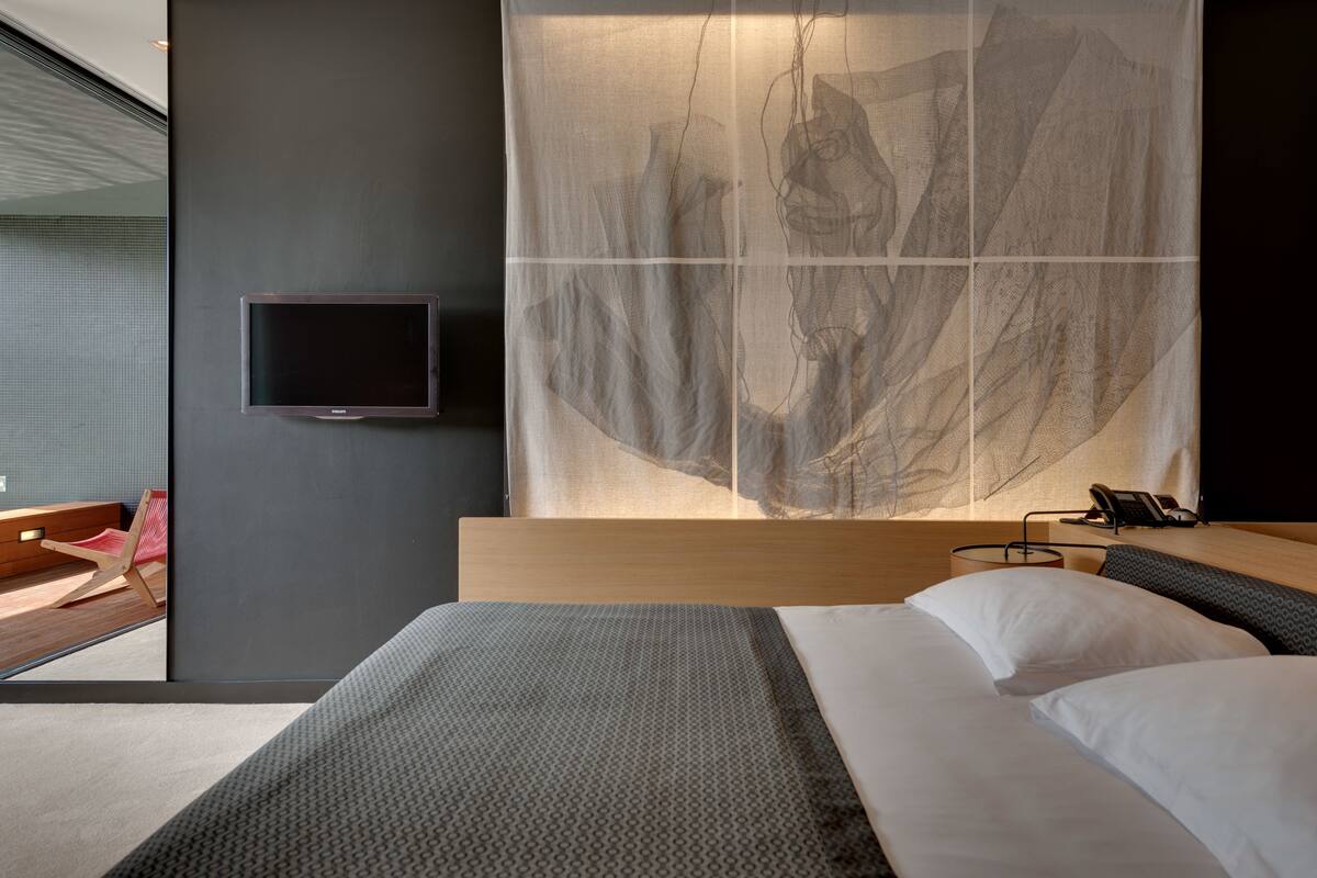 Una habitación de hotel moderna con una cama grande, un televisor de pantalla plana en la pared y una obra de arte abstracta de gran tamaño sobre la cama.