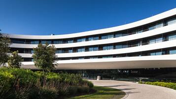 A modern building with a curved facade, multiple balconies, and a landscaped entrance area.