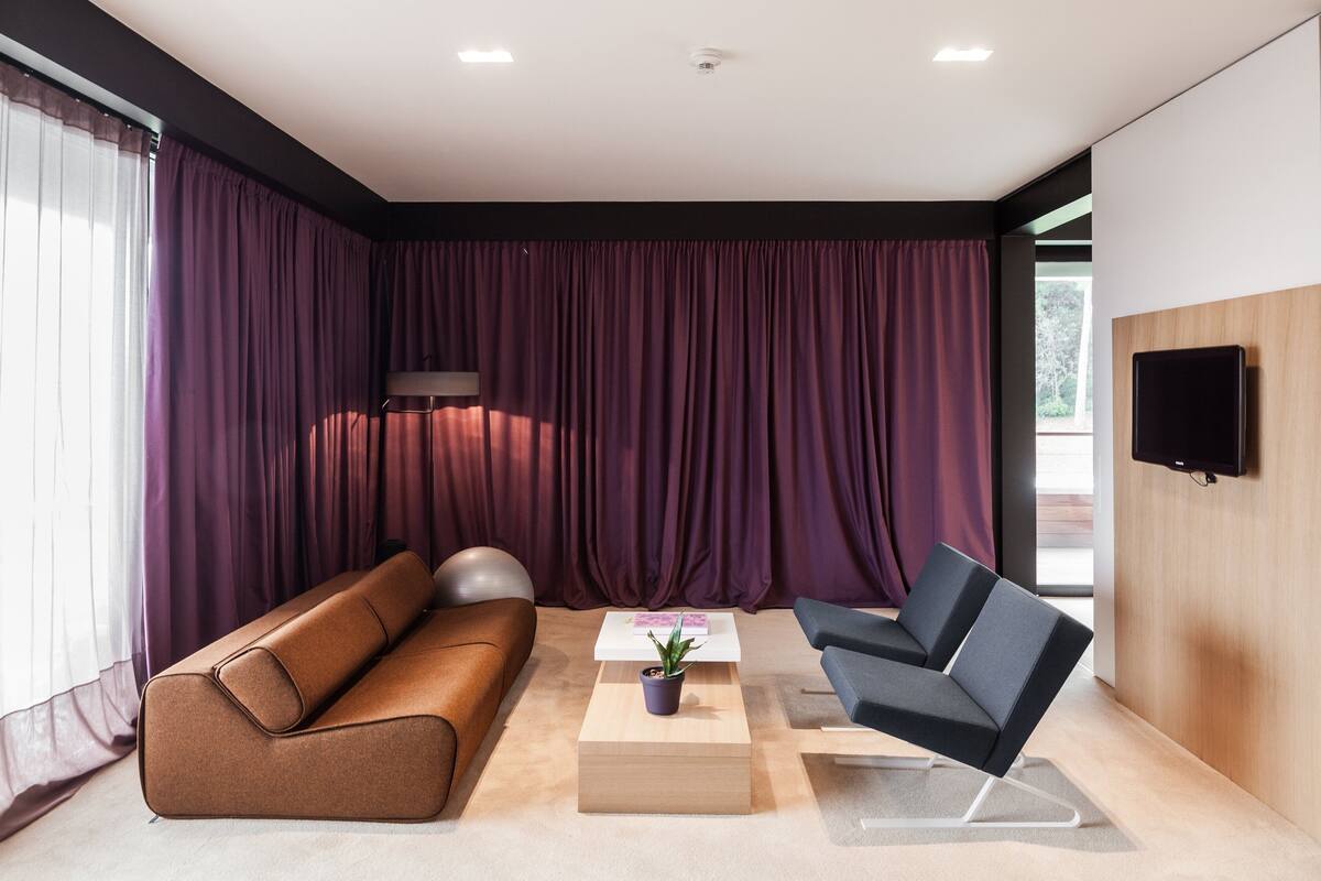 Una sala de estar moderna con un sofá marrón, un sillón azul, una mesita con una planta y un televisor fijado a la pared.