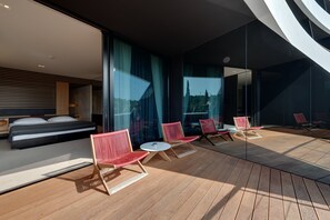 A modern hotel room with a large bed, a balcony with red chairs, and a view of the cityscape through large windows. - Lone Hotel by Maistra Collection (Rovinj)