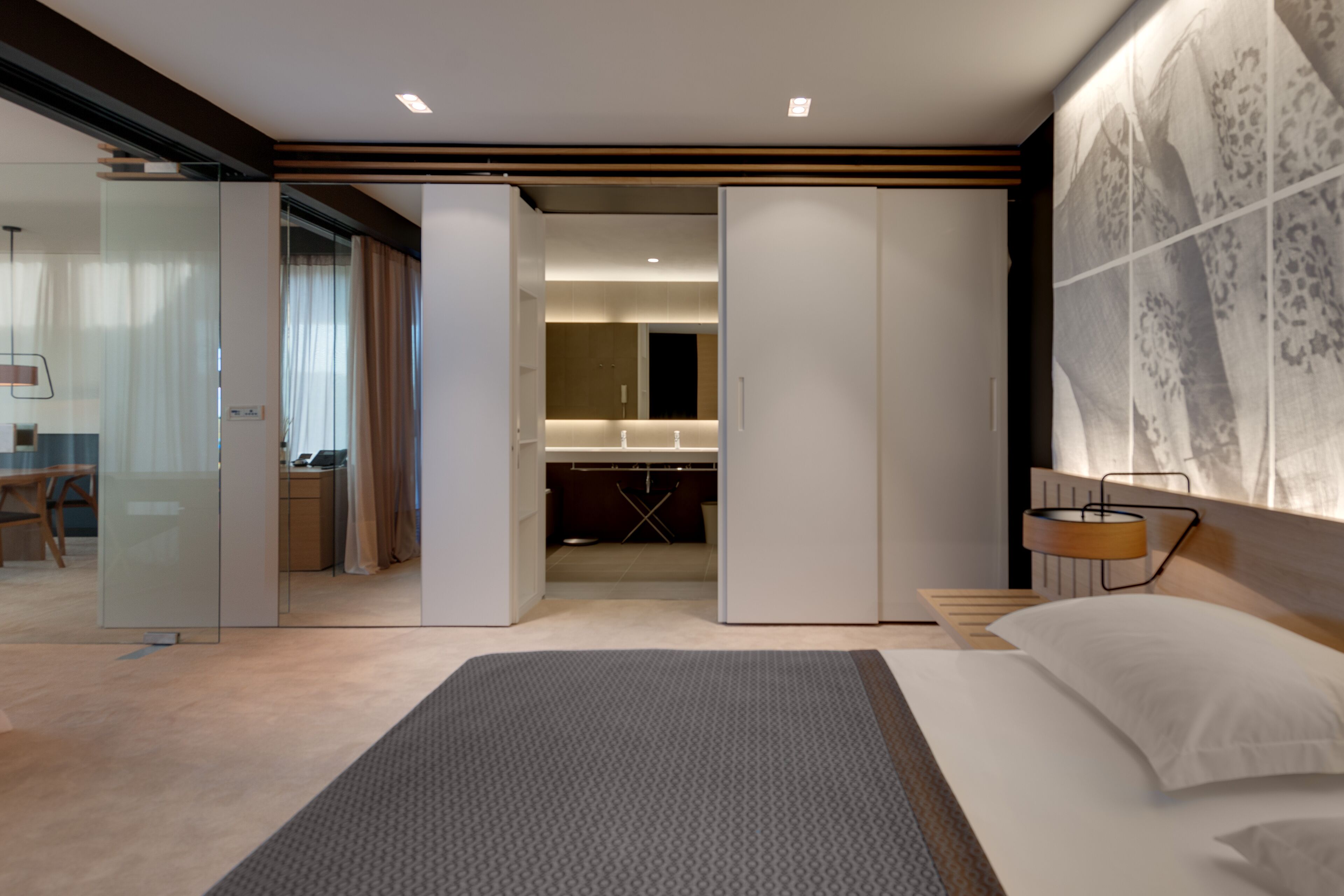 A modern hotel room with a large bed, a desk, a bathroom, and a sliding door leading to a balcony.