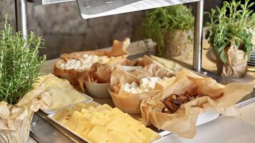 A buffet with various cheeses, meats, and pastries.