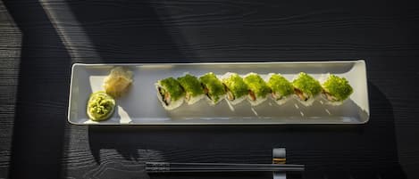A rectangular white plate with sushi on a dark wooden table.