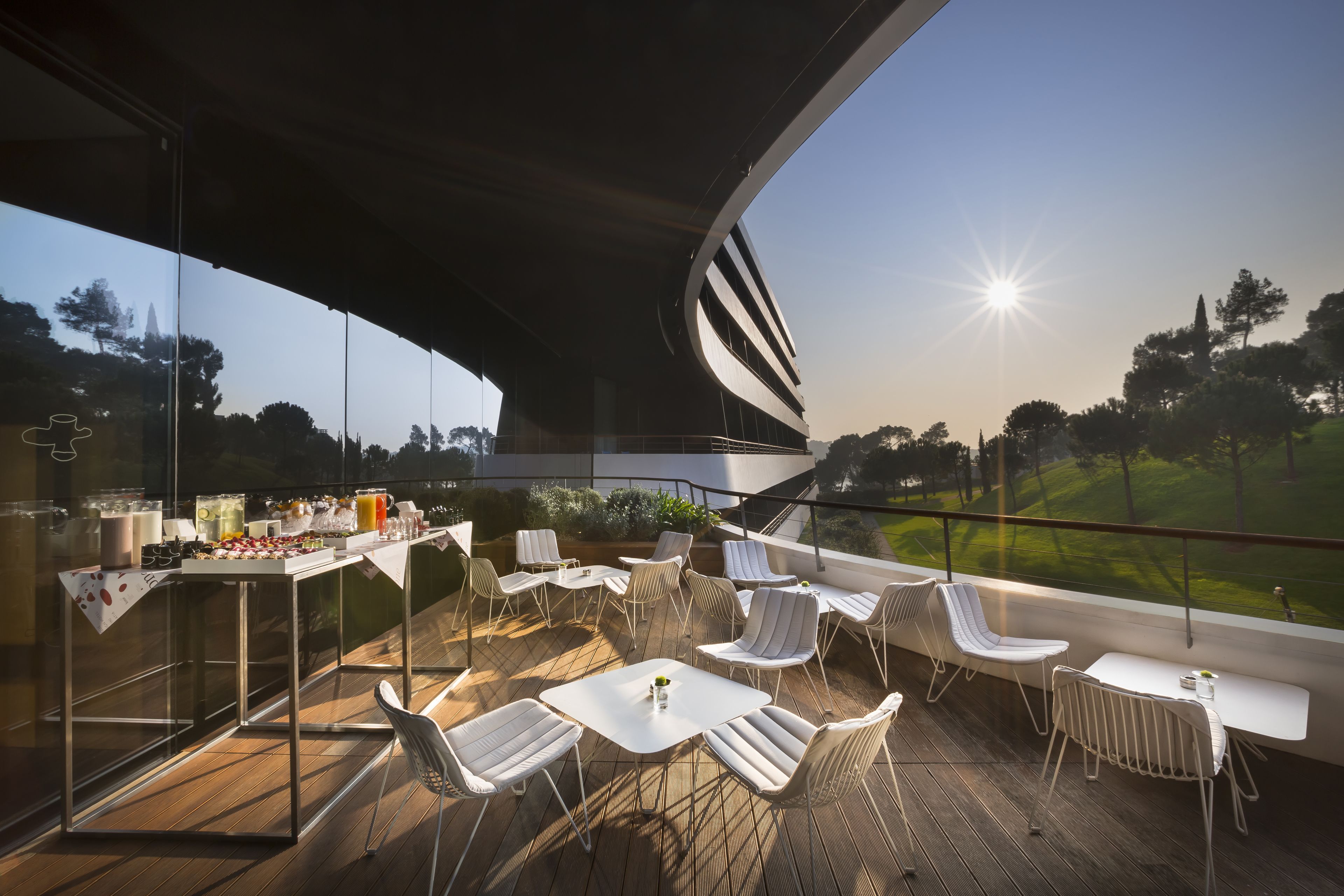 Une terrasse extérieure moderne, dotée de murs en verre, de mobilier blanc et offrant une vue sur un terrain de golf.
