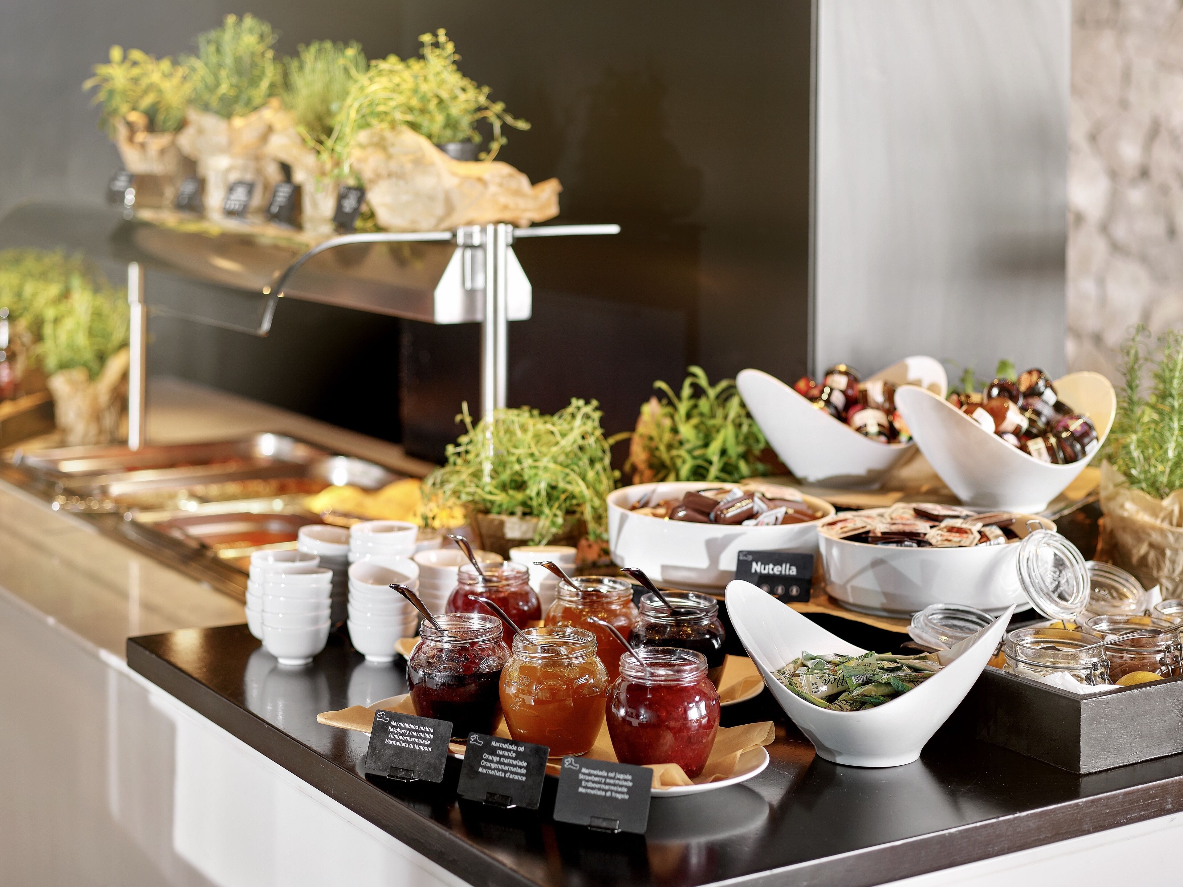 Un buffet proposant une variété d’aliments, notamment des pots de confiture, un bol de Nutella et un plateau de viennoiseries.