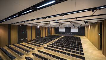A large auditorium with rows of black chairs and a stage at the front.