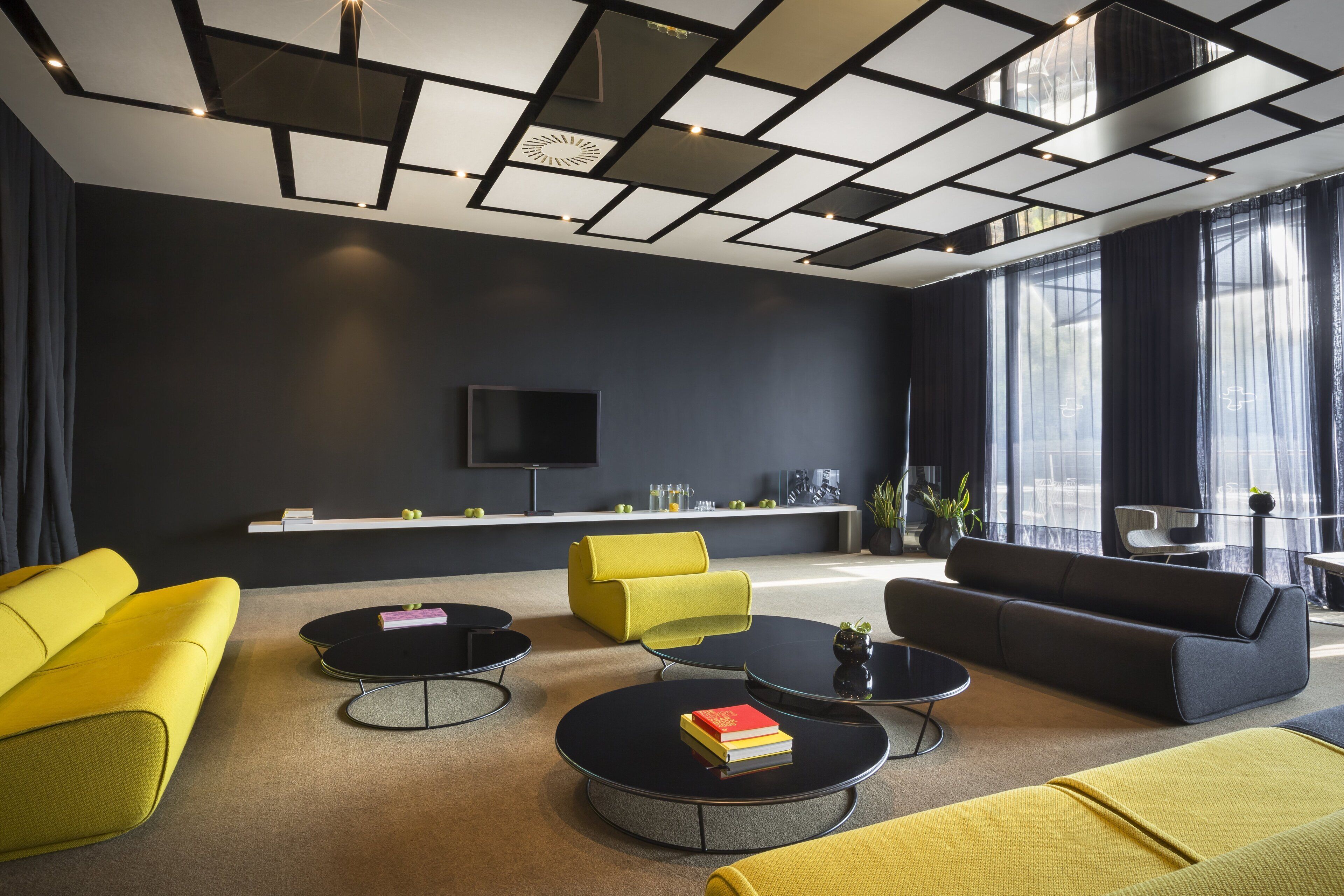 A modern living room with a flat-screen TV, yellow and black sofas, and a coffee table with books.