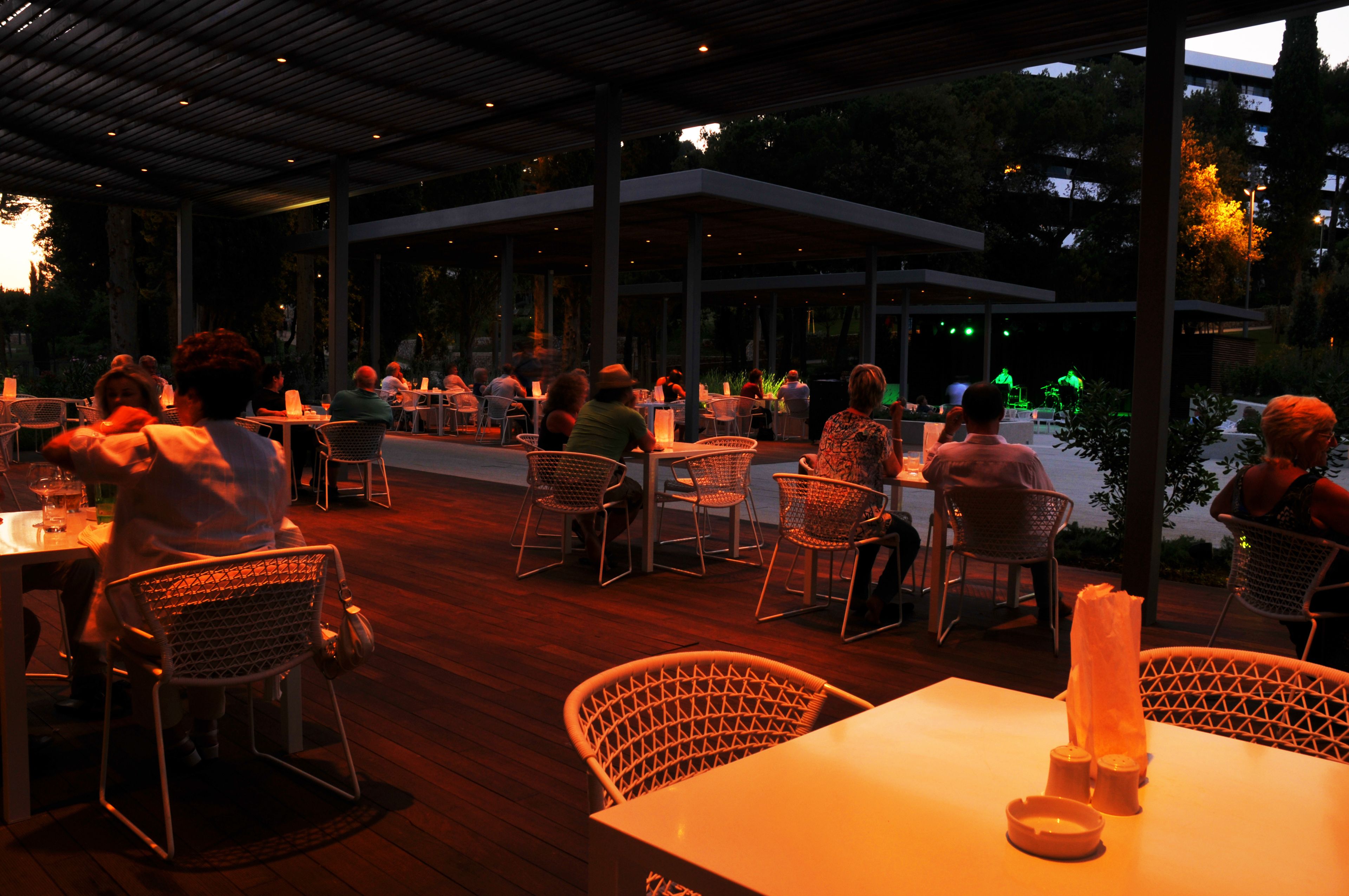 An outdoor dining area with tables and chairs, surrounded by a covered patio and a view of the cityscape.