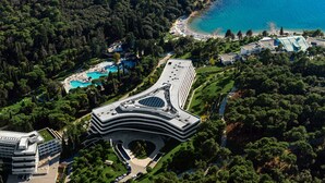 Vista aérea de un complejo turístico costero con un edificio de diseño curvo, una piscina y una playa.
