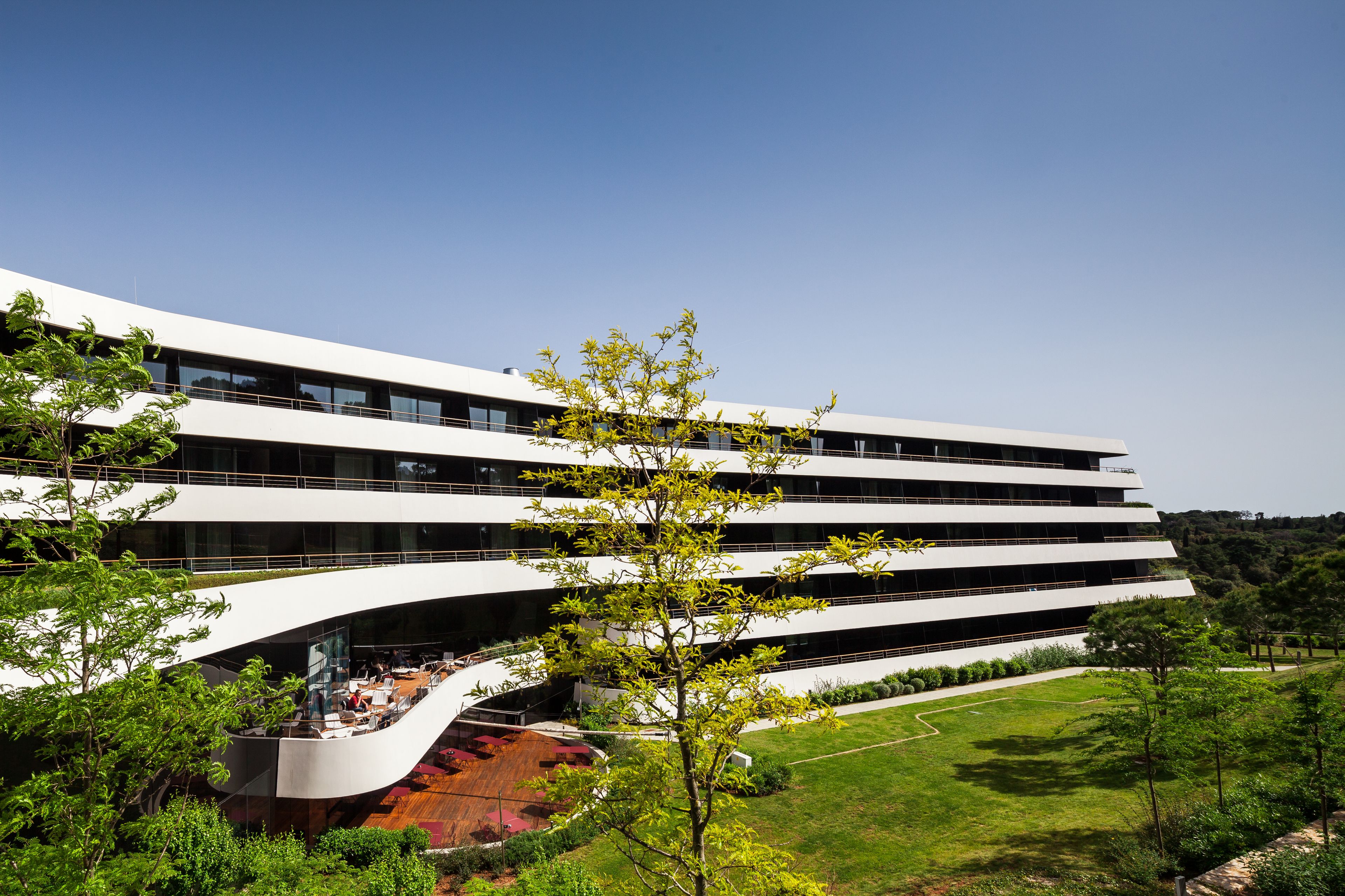 Un edificio moderno a più piani con facciata curva, area salotto esterna e un giardino curato.