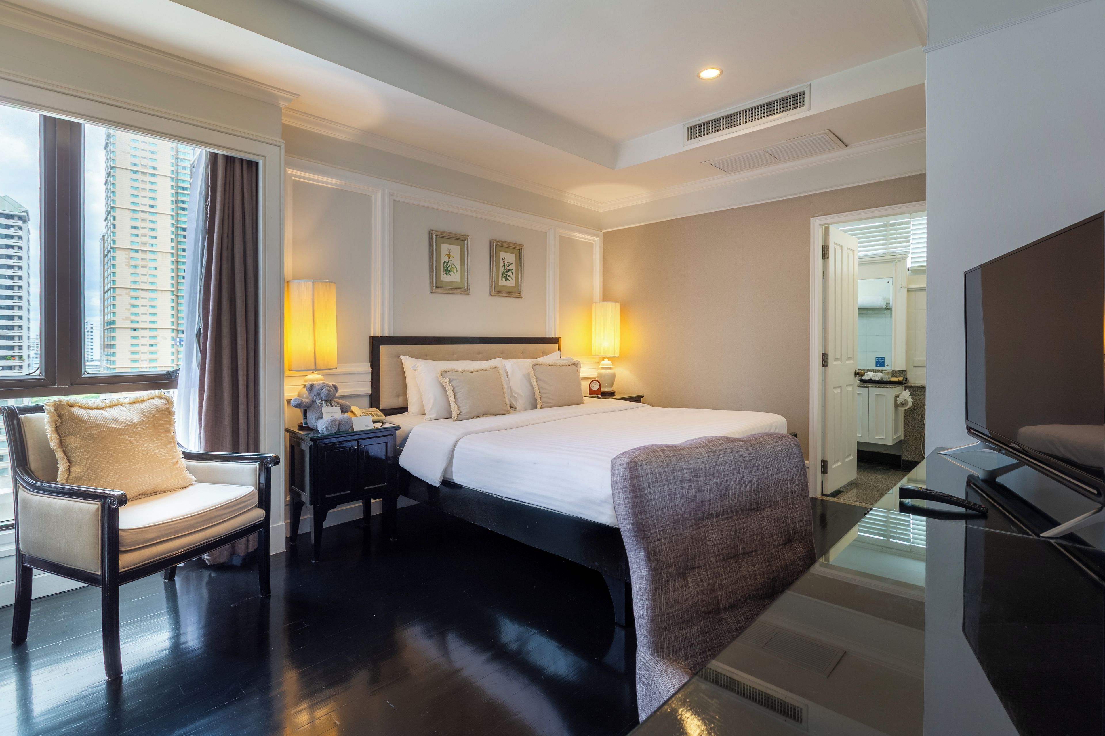 Une chambre d’hôtel comprenant un lit, des lampes de chevet, une chaise, un bureau et un téléviseur.