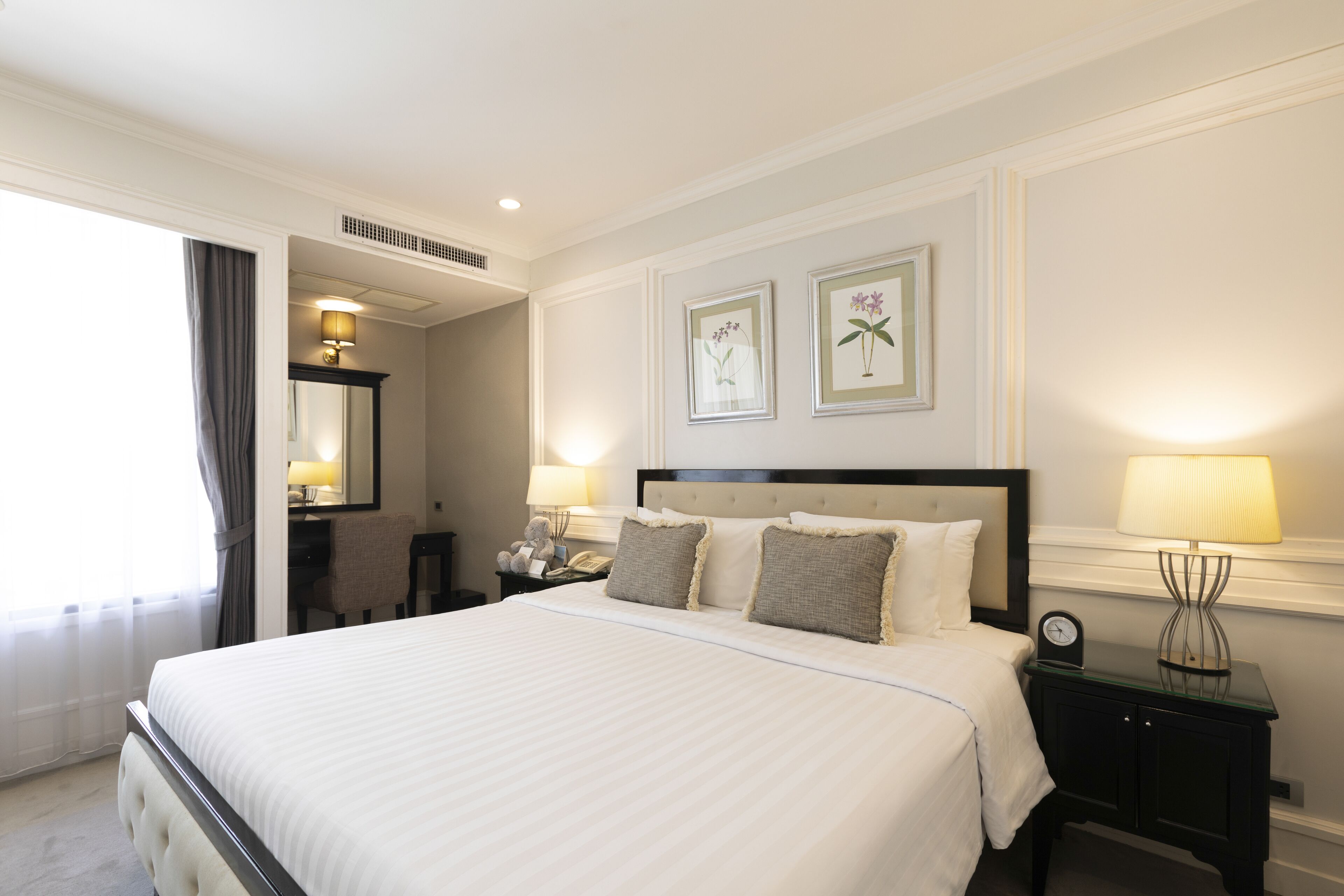 Habitación de hotel con una cama grande, una mesita de noche con lámpara, un escritorio con silla y arte botánico enmarcados en la pared.