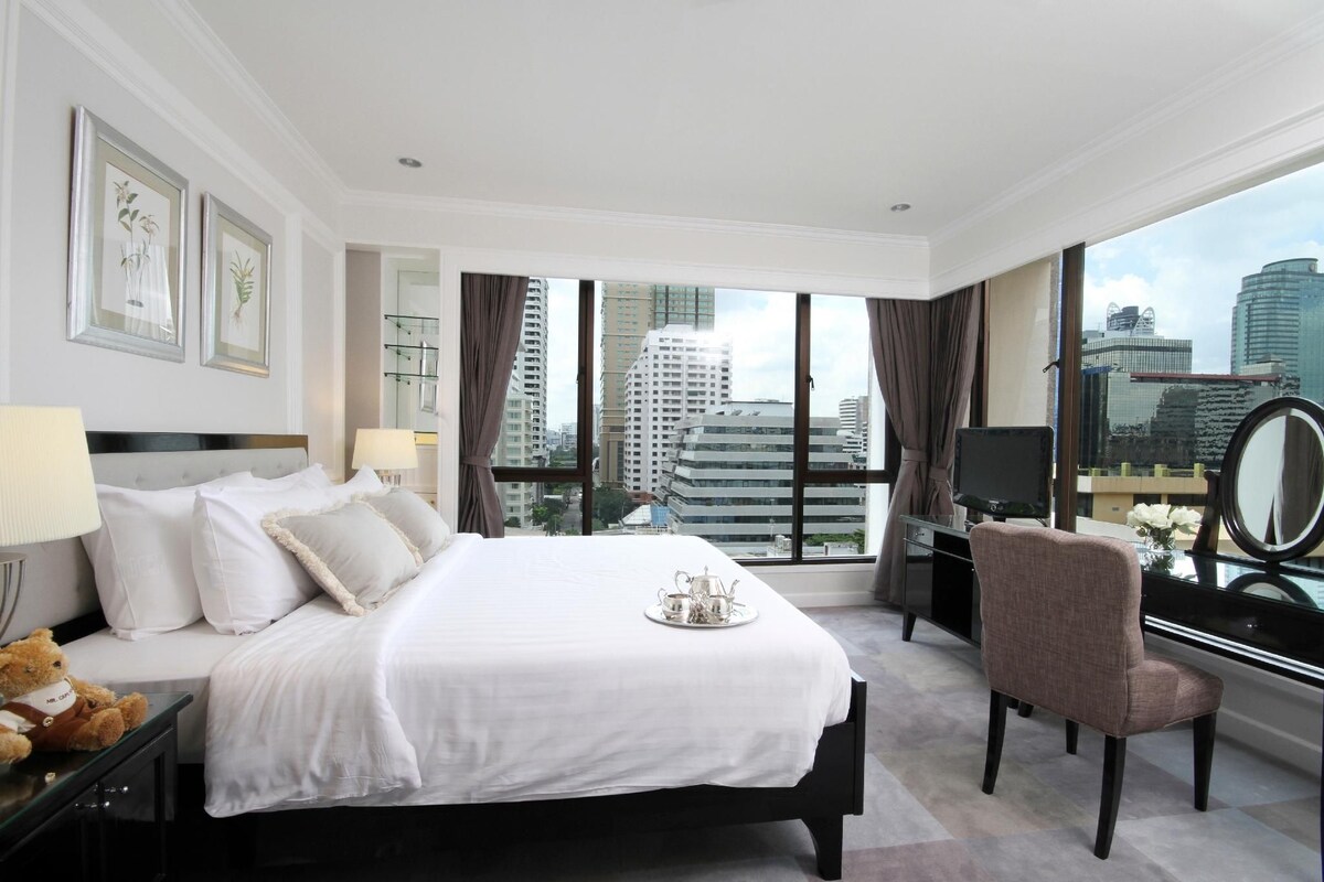 A hotel room with a large bed, a desk, a chair, and a view of the cityscape.