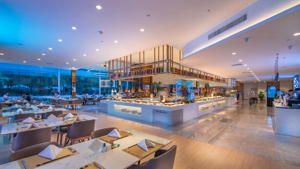 Un restaurant moderne doté d’un bar central, de plusieurs tables et offrant une vue sur l’extérieur.