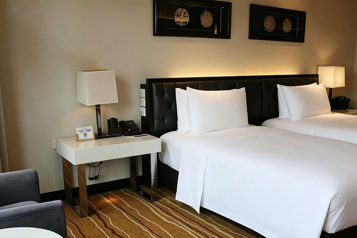 A hotel room with two beds, a desk with a telephone, a chair, and a carpeted floor.