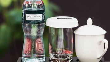 A bottle of water, a glass, and a white mug on a tray.
