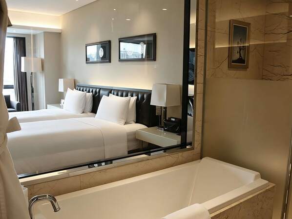 Habitación de hotel con dos camas, un espejo grande, una bañera y obras de arte en las paredes.