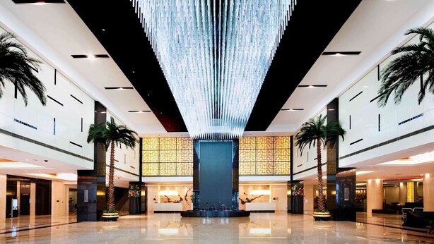 En rummelig lobby med en moderne lysekrone, palmer og en receptionsdisk.