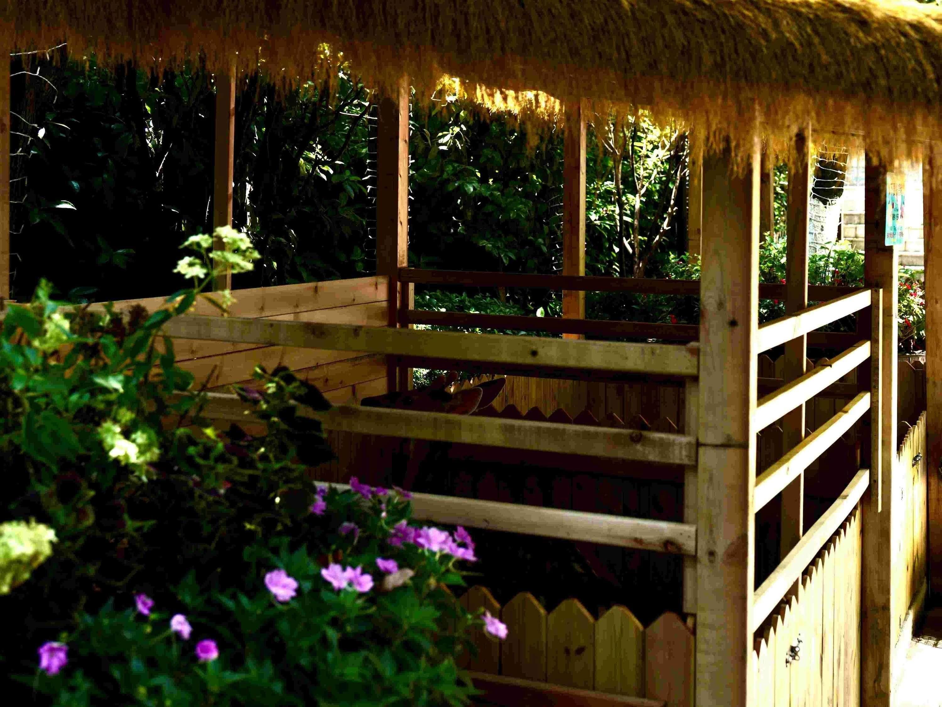 A wooden structure with a thatched roof, surrounded by greenery and flowers.