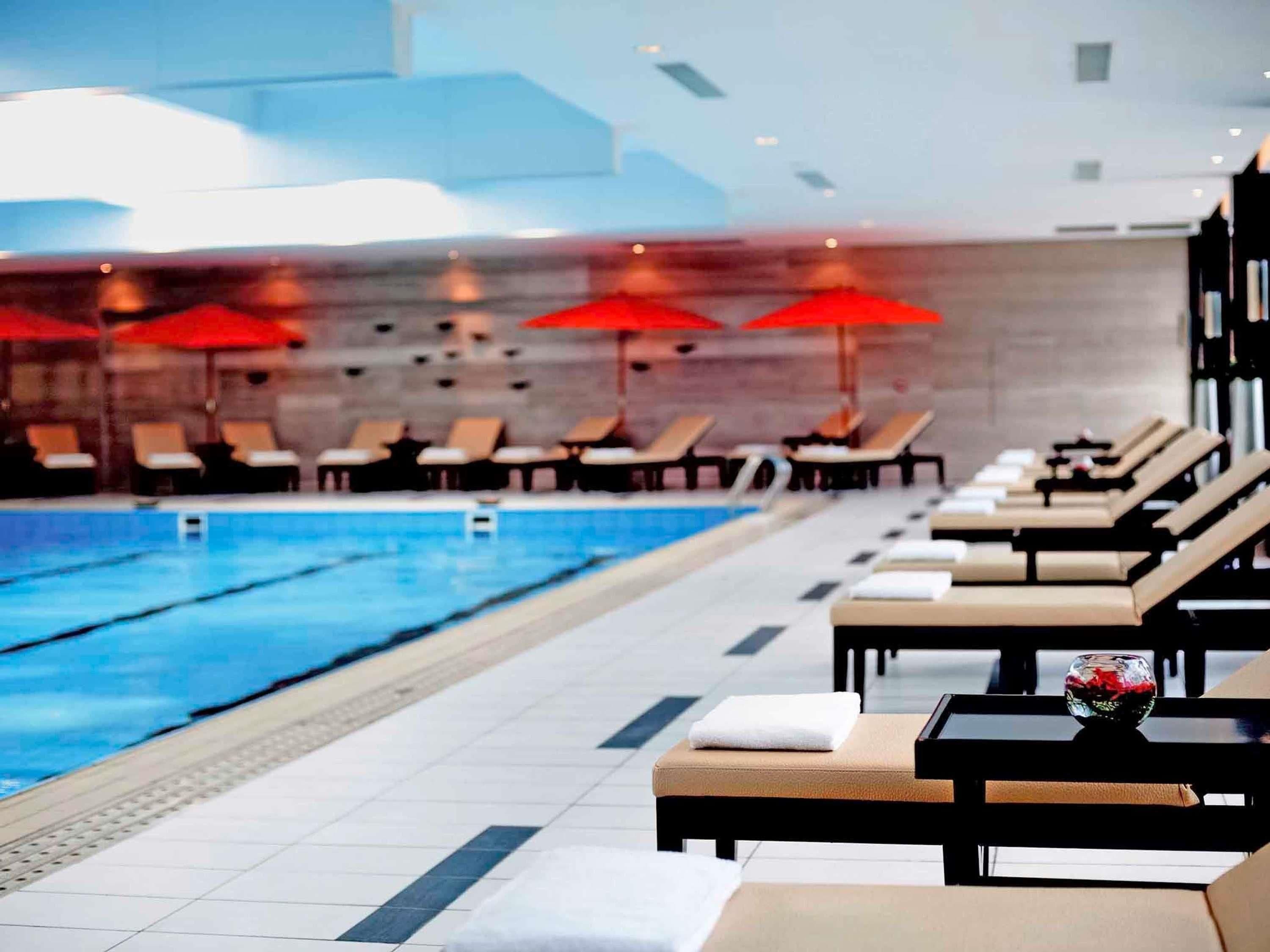 A swimming pool with lounge chairs and umbrellas, a tiled floor, and a modern interior design.