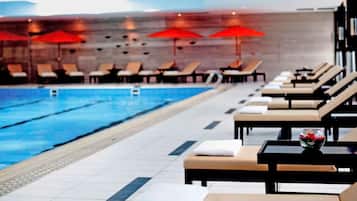 A swimming pool with lounge chairs and umbrellas, a tiled floor, and a modern interior design.