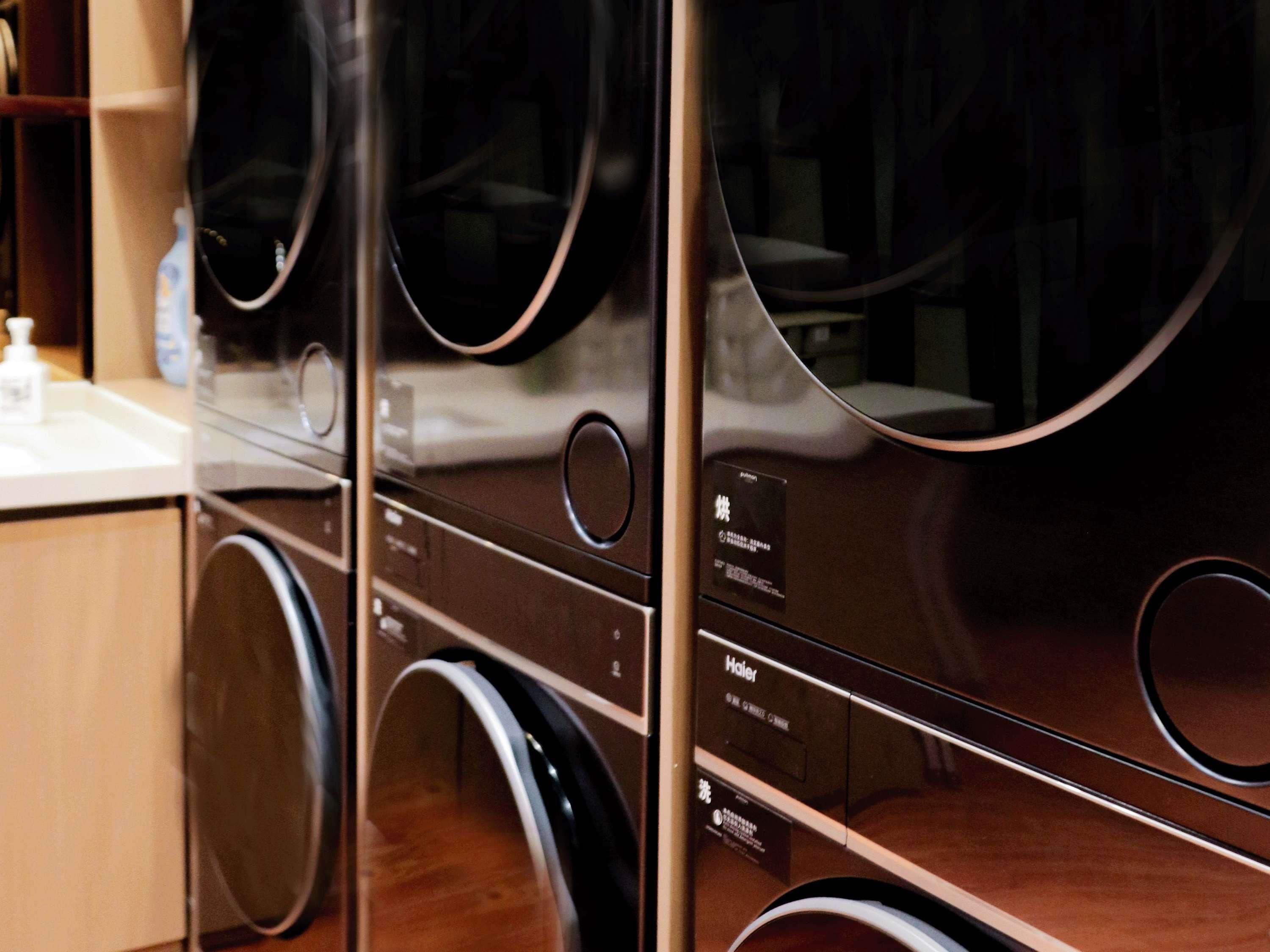 A row of front-loading washers with control panels, a wooden countertop, and a bottle of hand soap.