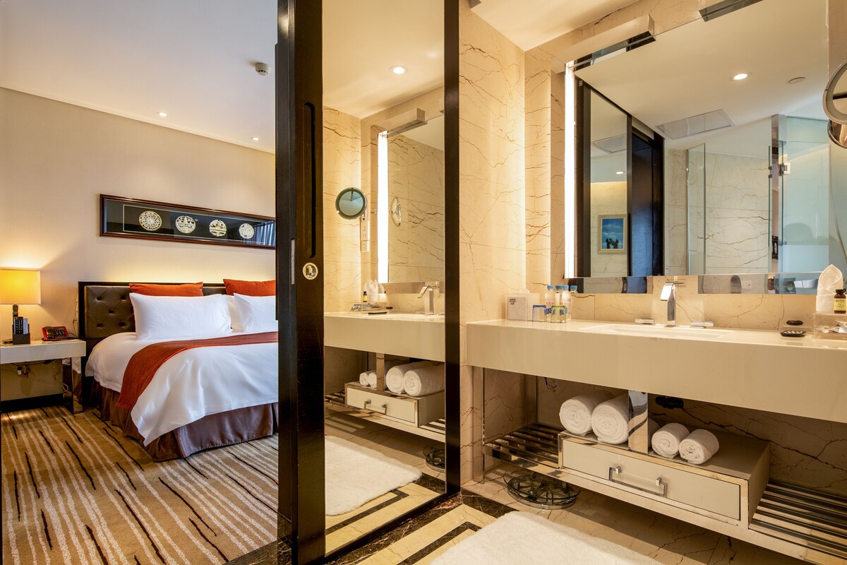 Habitación de hotel con cama, baño con un espejo grande y una obra de arte colgada en la pared.