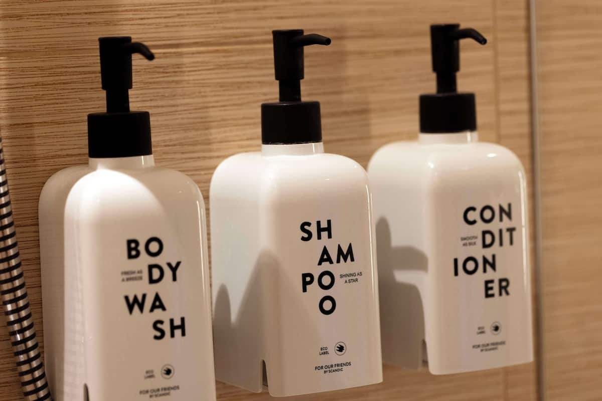 Three bottles of body wash, shampoo, and conditioner on a wooden shelf.