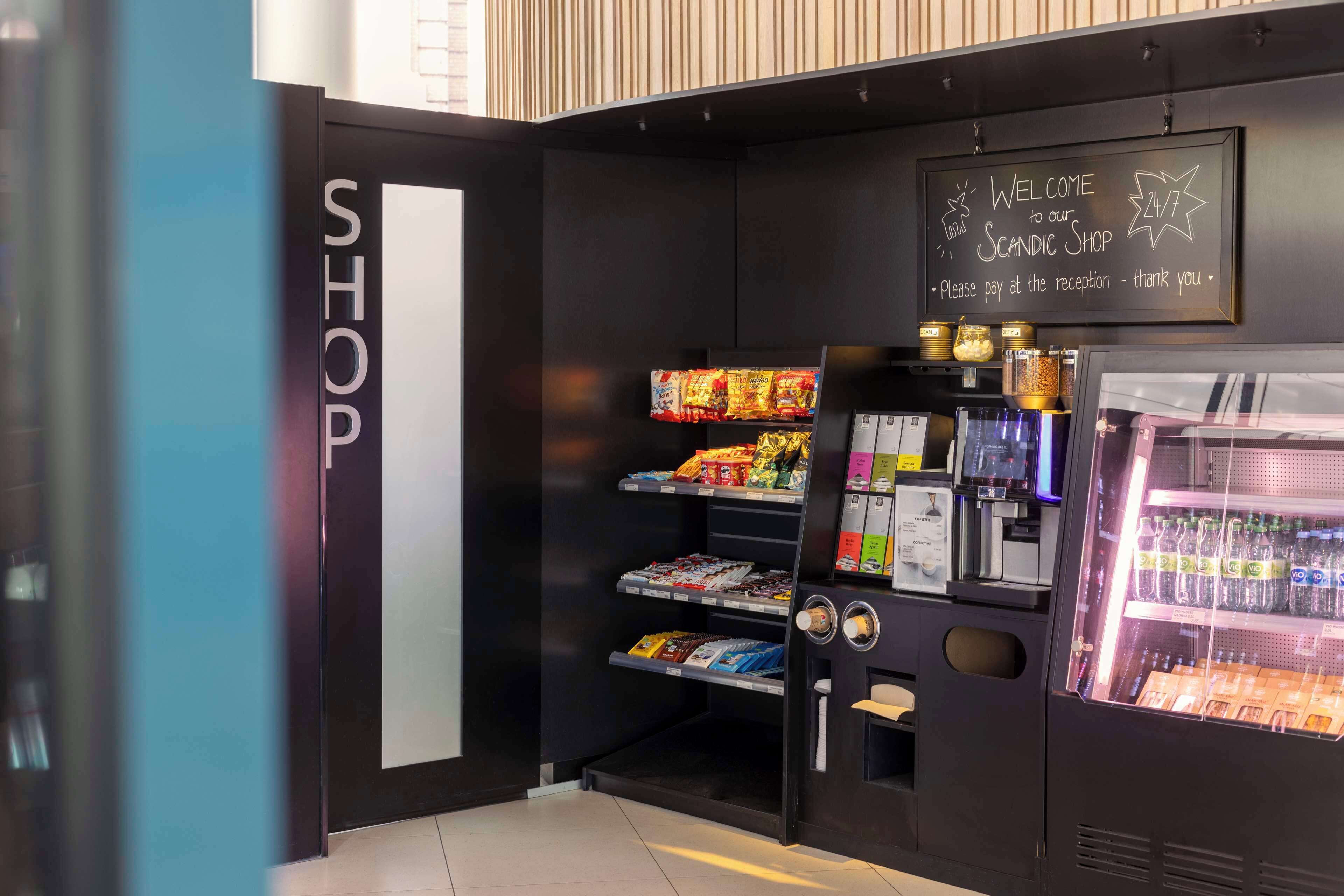 A modern shop with a black and white color scheme, featuring a cash register, shelves stocked with snacks, and a refrigerated display case.
