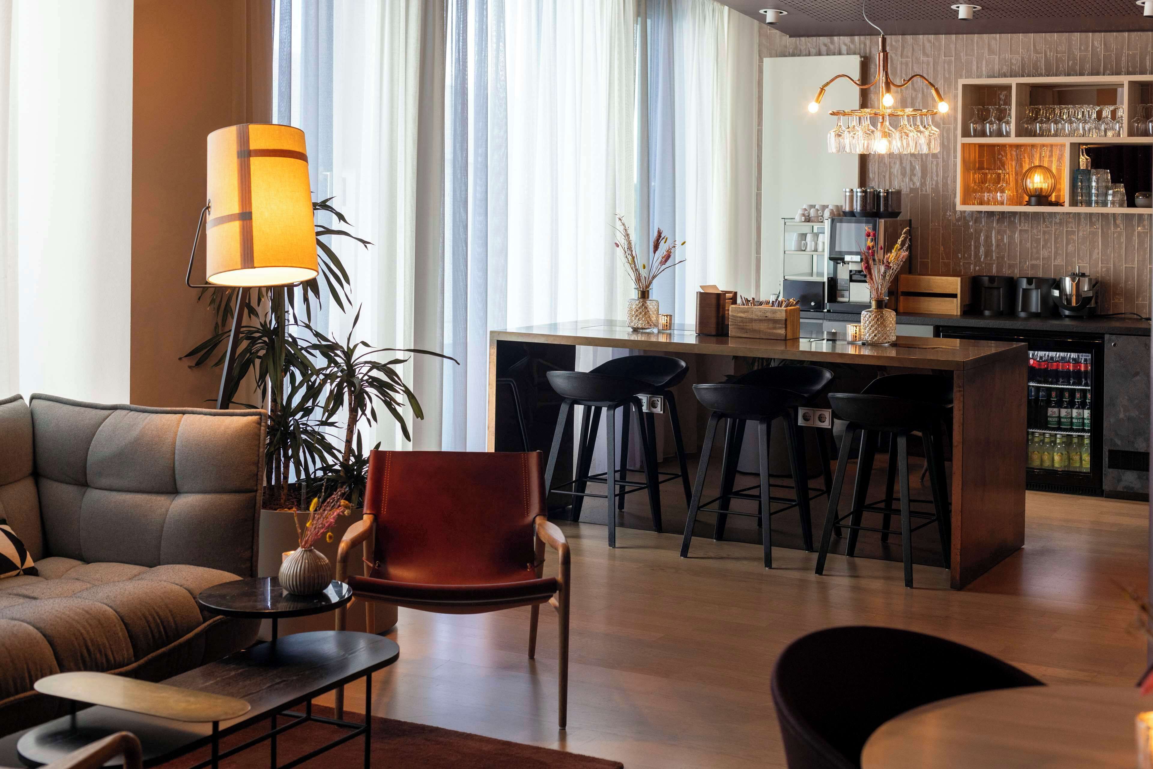 Una sala moderna con sofá, una mesa de centro y una silla roja. Se observa una zona de cocina con barra y taburetes.