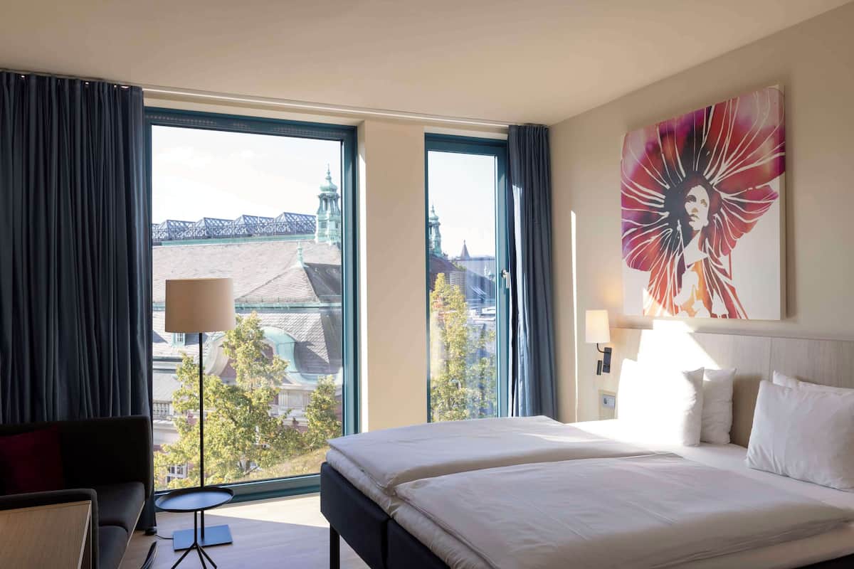 A hotel room with a large bed, a desk, a chair, a lamp, and a painting.