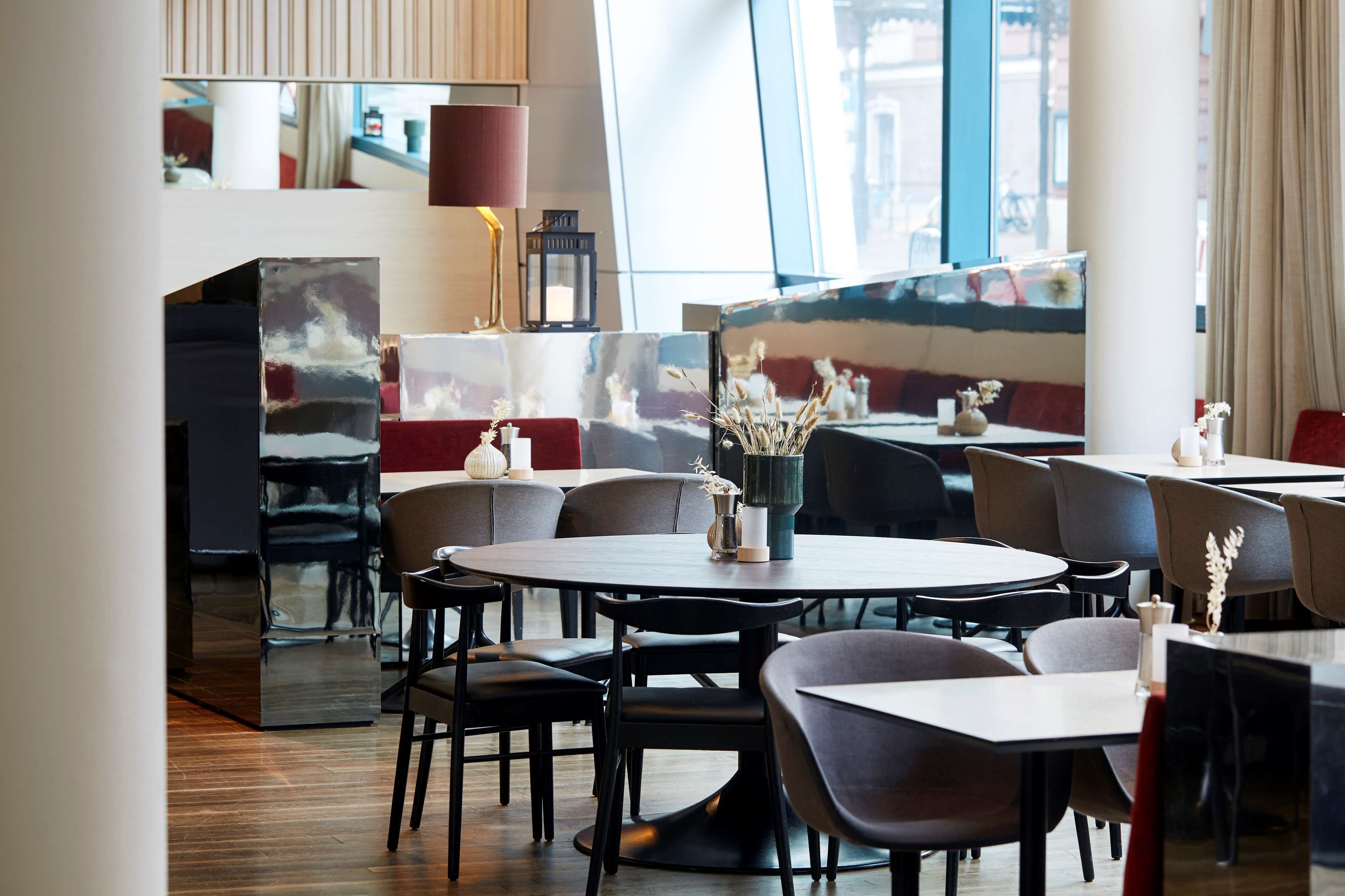 A modern restaurant interior with round tables, dark chairs, and a mix of red and grey seating.