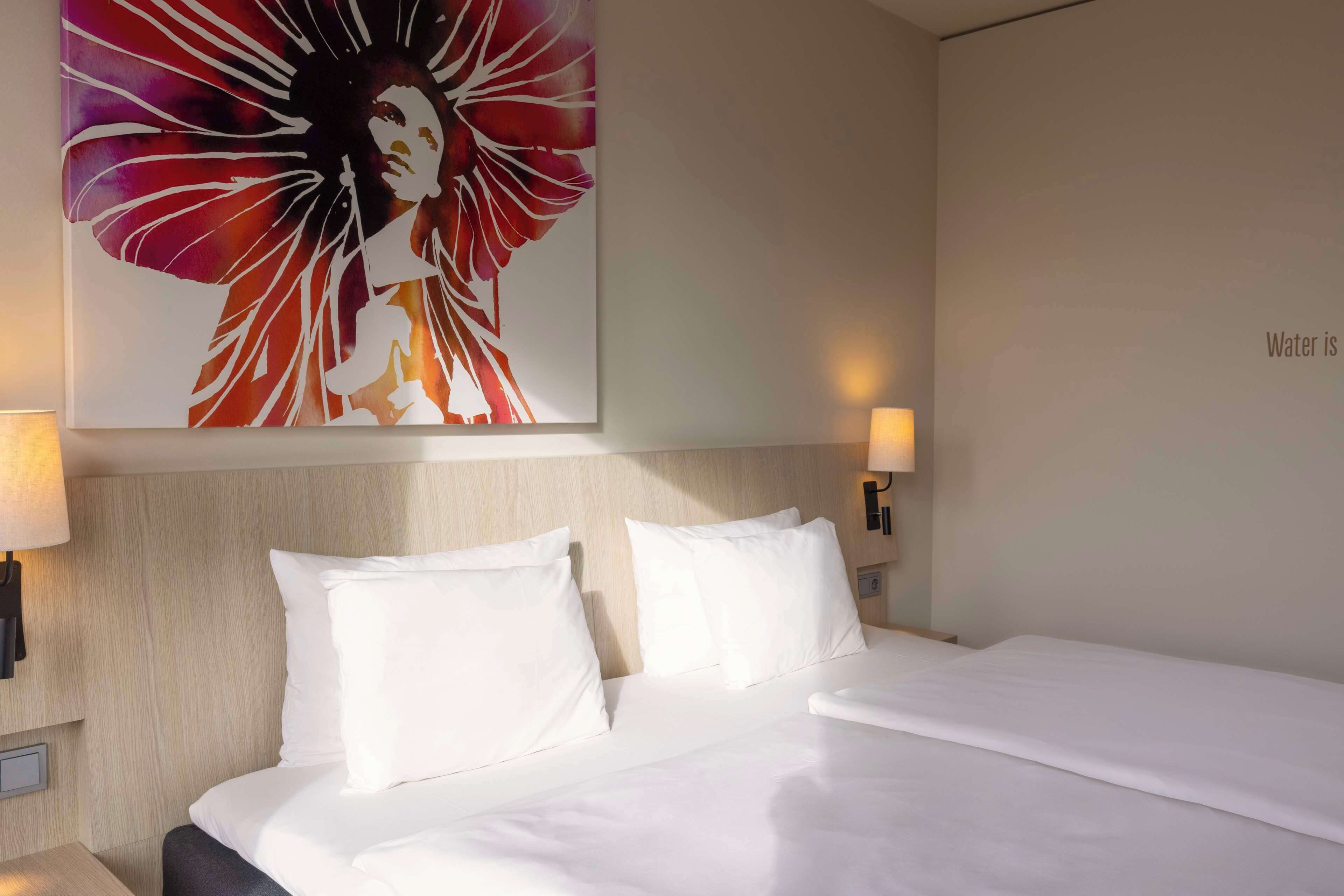 Ein Hotelzimmer mit einem großen Bett, zwei weißen Kissen, einer Kopfteil und zwei Wandleuchten.
