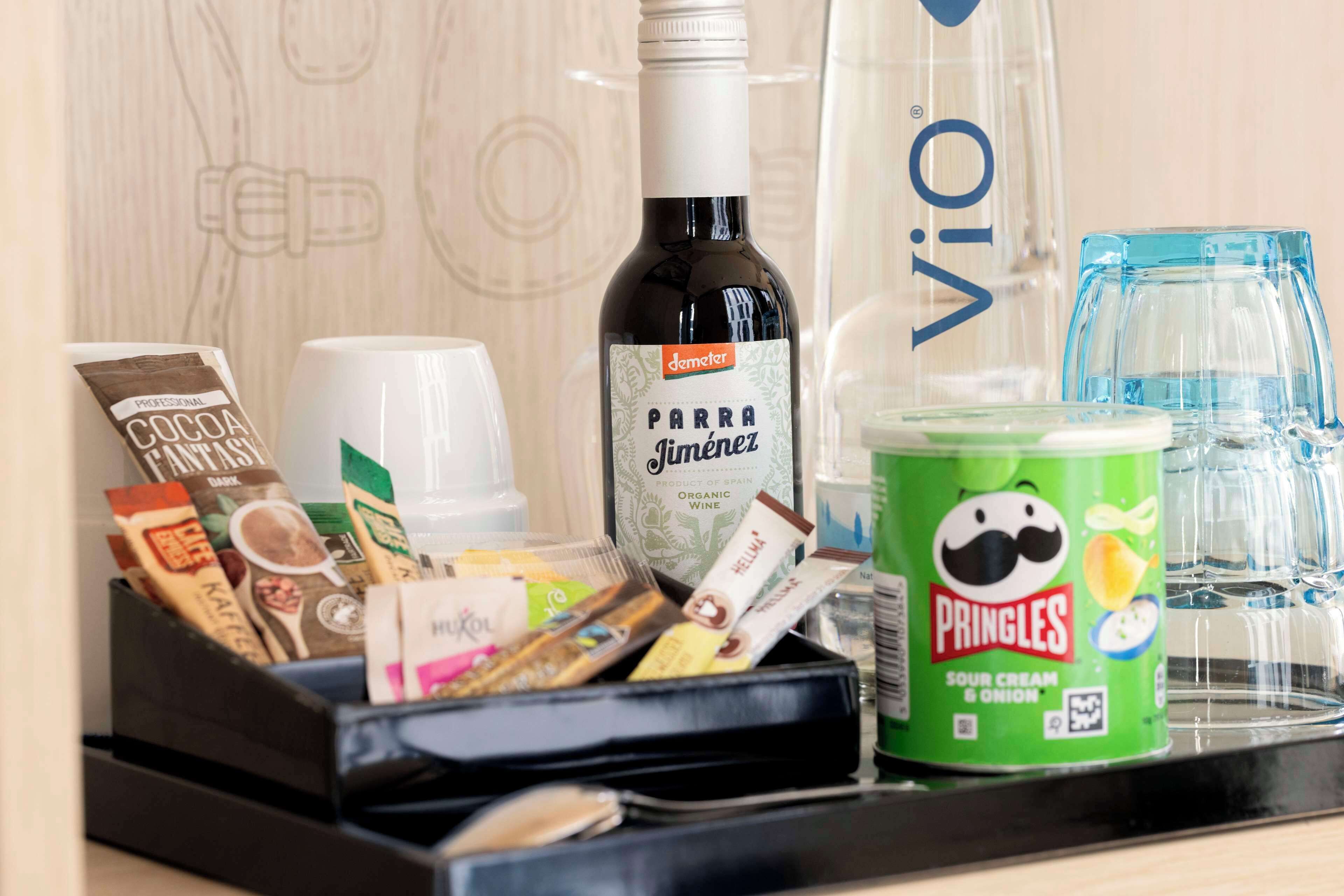 A minibar with a bottle of Parra Jimenez wine, Pringles snacks, and various coffee packets.