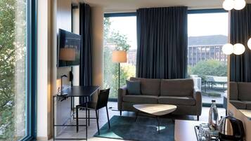 Ein modernes Hotelzimmer mit einer Sitzecke, einem Couchtisch, einem Fernseher und einem Essbereich mit Tisch und Stühlen.