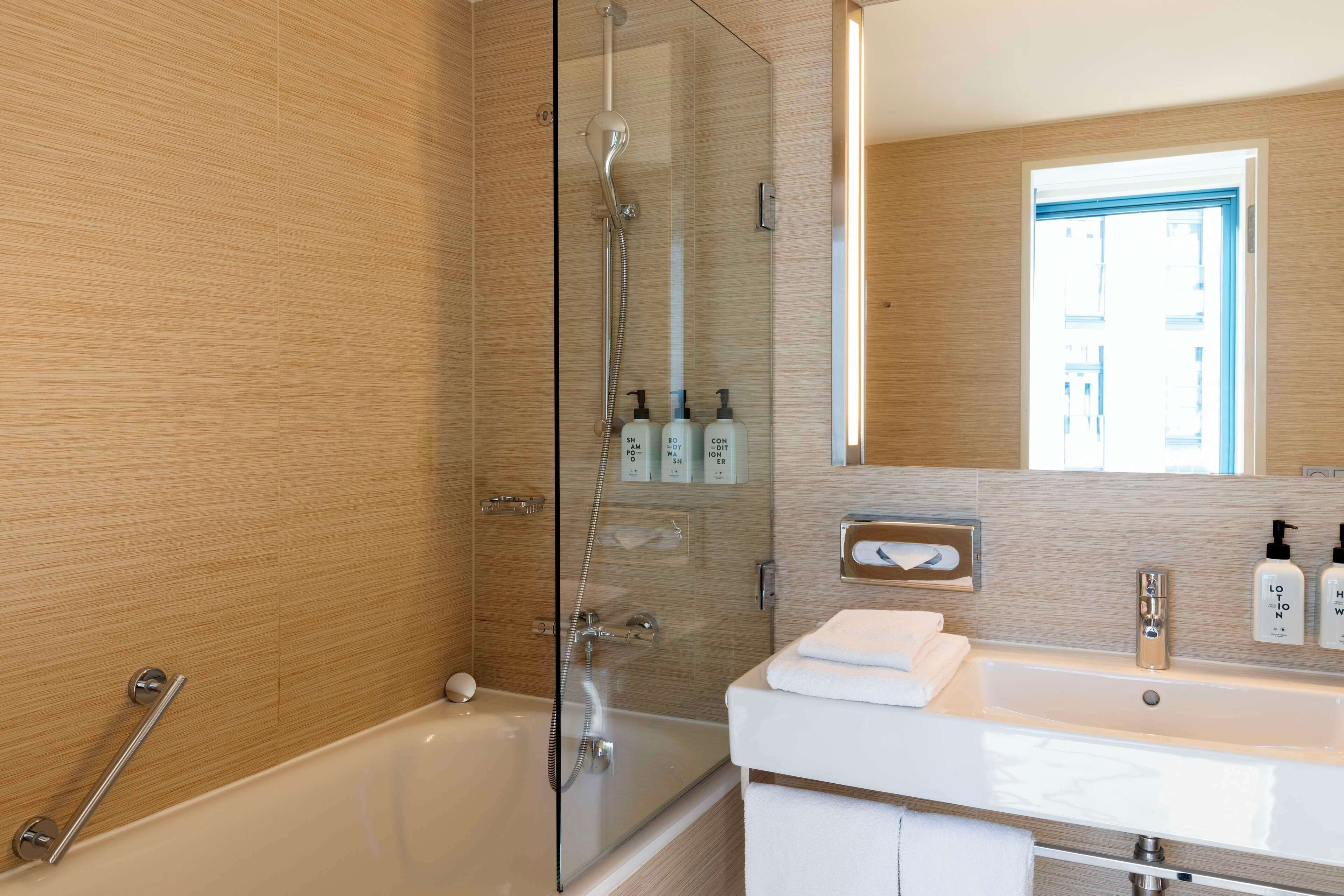 A modern bathroom with a glass-enclosed shower, a bathtub, and a vanity with a sink and mirror.